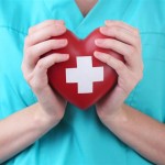 Red heart with cross sign in doctor hand, close-up, isolated on white